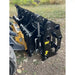 Black steel clam grapple attachment with hydraulic cylinders and mounting points resting on dirt and leaves outdoors