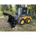 Yellow John Deere skid steer loader with black hydraulic grapple attachment outdoors on grass and dirt near trees