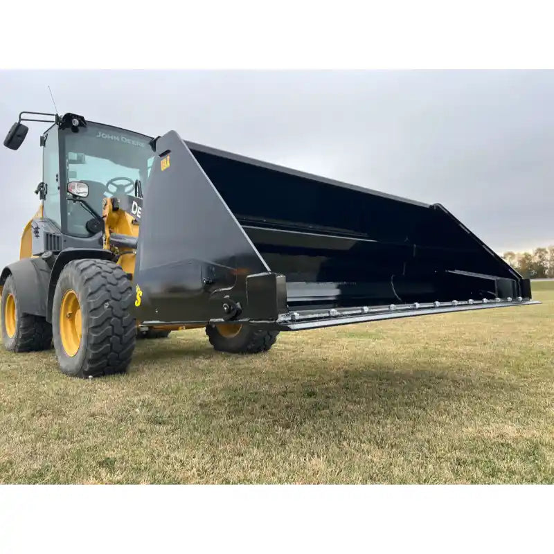 Front view of black steel tractor hydraulic dump bucket attachment raised on yellow loader on grass field