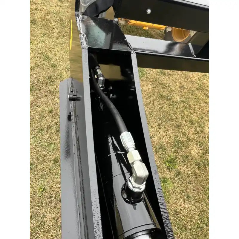 Close-up of black painted hydraulic hose and metal fitting inside steel frame of attachment over dry grass surface