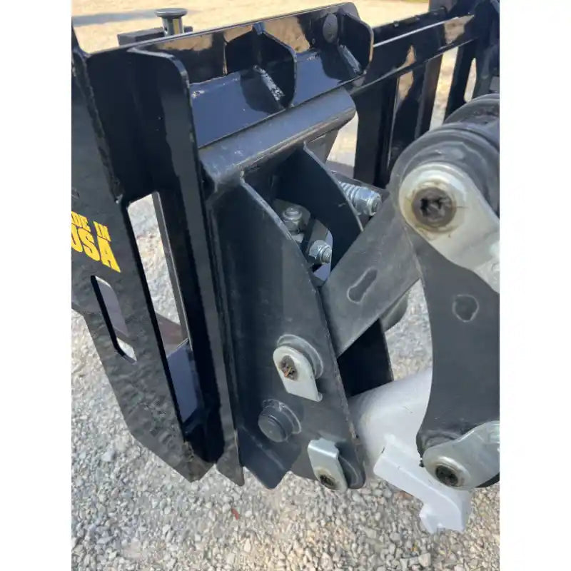 Close-up of black steel skid steer attachment plate with mounting hardware and bolts on gravel surface outdoors