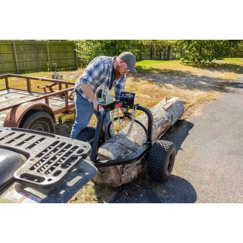 Operator using Swisher ATV log skidder with hand crank winch to lift large log on paved surface, gallery position 1