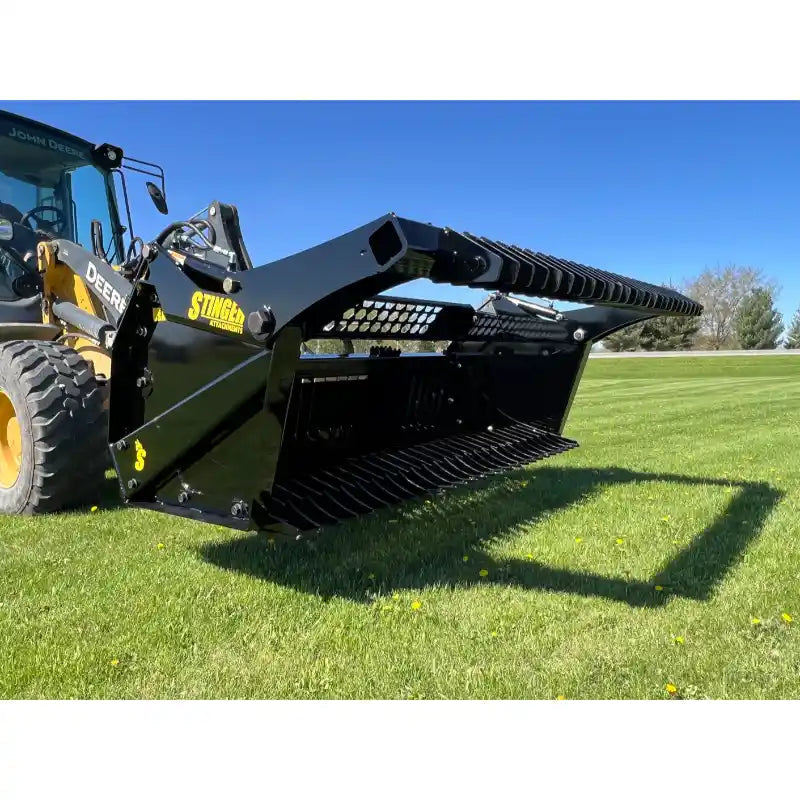 Front-right view of skid steer with black Stinger rock bucket reel attachment on green grass under clear sky