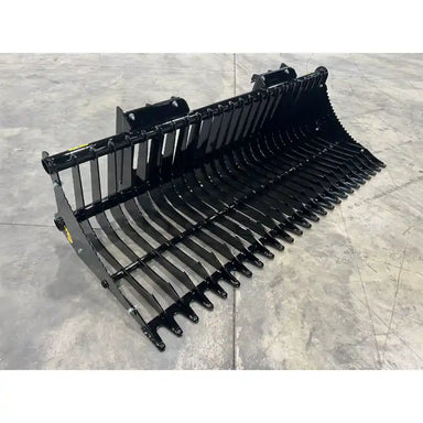 Black metal rock bucket attachment with curved tines and reinforced mounting brackets on concrete floor surface