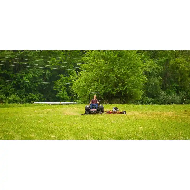 Zero-turn mower cutting a grassy field with trees in the background, mower centered, gallery position 1