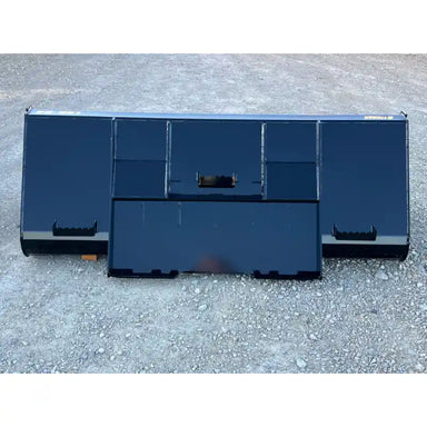 Front view of a black steel liquid slurry bucket attachment resting on gravel surface outdoors