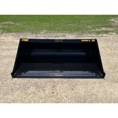 Front view of black skid steer material bucket with smooth interior and yellow Series 3 78 decals on gravel surface