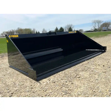 Black steel skid steer bucket with smooth interior, reinforced cutting edge, and yellow Stinger labels on gravel surface outdoors