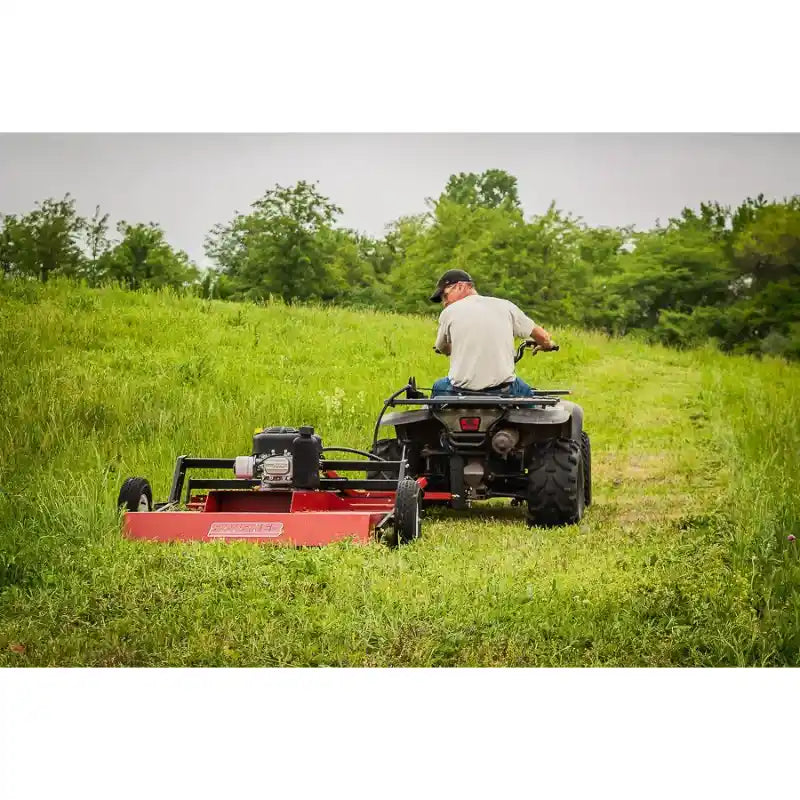 Rear view of ATV towing red Swisher 44" Rough Cut Brush Mower across grassy field, gallery position 1