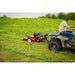 Side view of green ATV towing red Swisher 44" rough cut mower across freshly cut grassy field, gallery position 1
