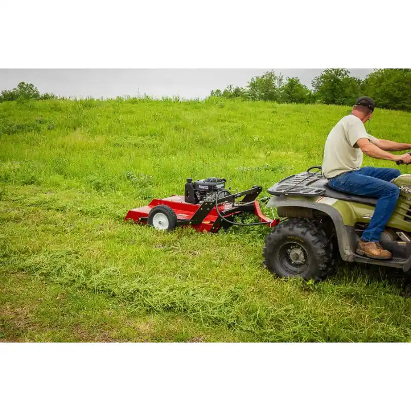Side view of green ATV towing red Swisher 44" rough cut mower across freshly cut grassy field, gallery position 1