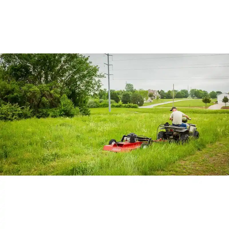 Rear view of ATV towing red Swisher 44" rough cut brush mower across tall grass, gallery position 1