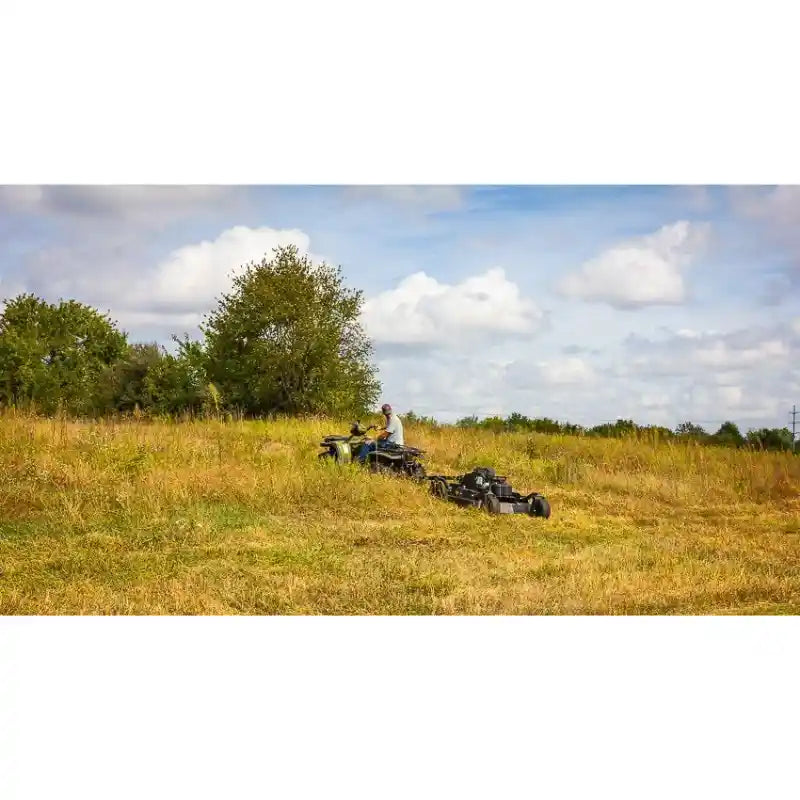 Person operating ATV towing Swisher 44" rough cut brush mower across uneven grassy field, gallery position 1