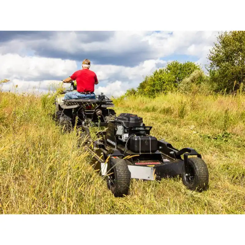 Tow-behind Swisher 44-inch brush cutter with Kawasaki 14.5HP engine attached to ATV cutting overgrown grass, gallery position 1