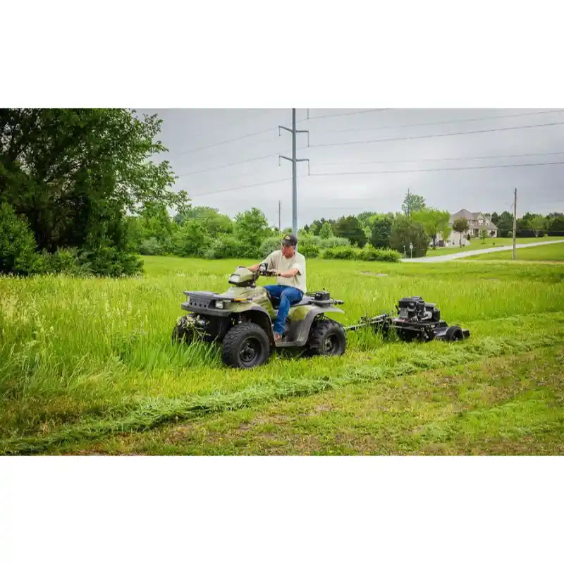 Man on ATV towing Swisher 44" rough cut mower across tall grass in rural setting, gallery position 1