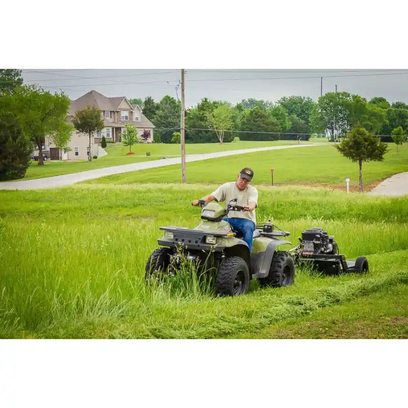 Operator riding ATV towing Swisher 44-inch rough cut mower cutting tall grass in residential area, gallery position 1