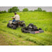 A person operates an ATV pulling a Swisher 44 Rough Cut Mower – 14.5HP 12V Country Cut, effectively mowing tall grass in a field with trees in the background.