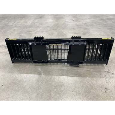 Wide black skid steer rock bucket attachment with solid side panels and reinforced back plates on concrete floor