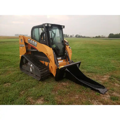 Yellow tracked skid steer loader with black stump bucket attachment on grassy field under cloudy sky