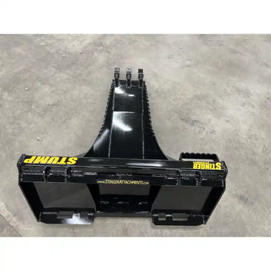 Black steel skid steer stump bucket attachment with reinforced cutting edge and mounting brackets on concrete floor indoors