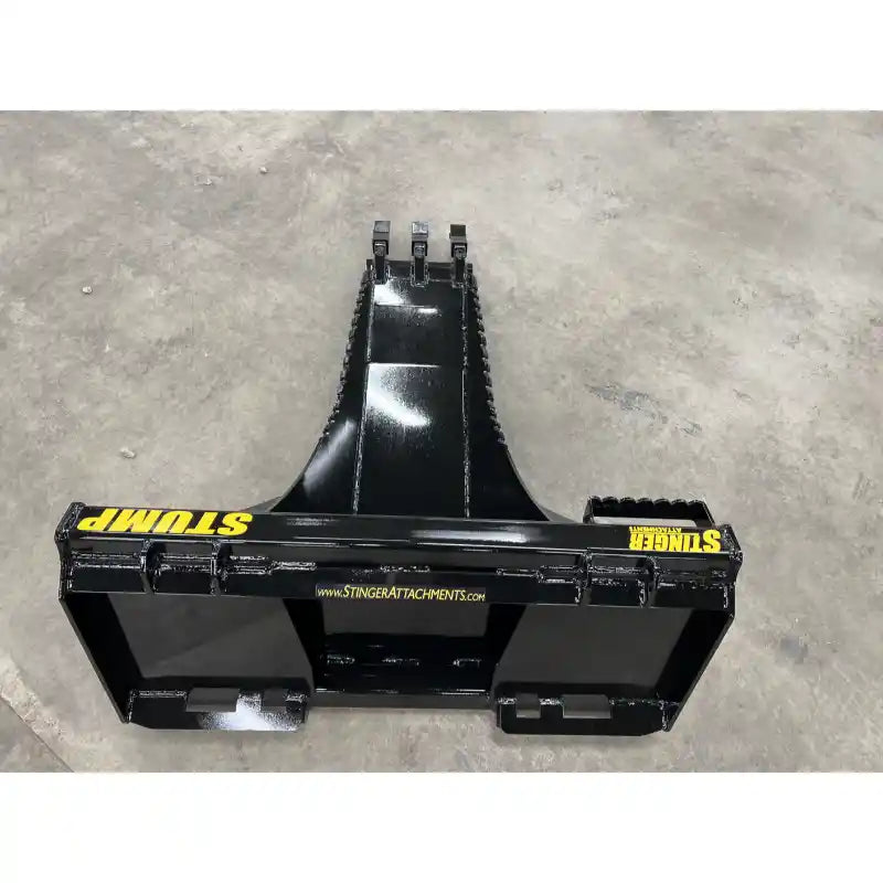 Black steel skid steer stump bucket attachment with reinforced cutting edge and mounting brackets on concrete floor indoors
