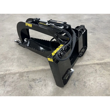 Black skid steer stump bucket grapple attachment with hydraulic cylinders and reinforced mounting frame on concrete floor