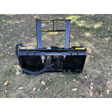 Black steel tractor-mounted tree puller attachment with reinforced frame and hydraulic hose on grass terrain