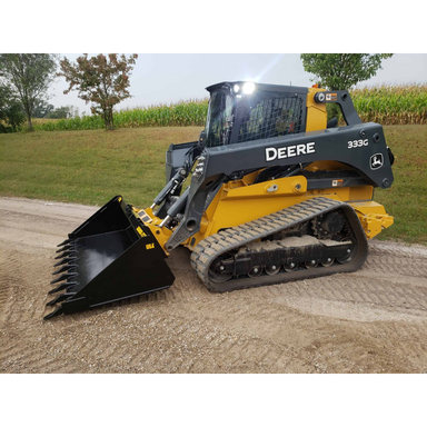 Yellow and gray compact track loader with toothed black bucket attachment on gravel path near grass and trees