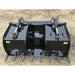 Black steel demolition grapple bucket with dual hydraulic cylinders and teeth resting on gravel surface outdoors