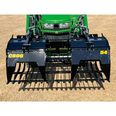 Black steel rock grapple attachment with wide spaced tines and dual hydraulic arms on grass field
