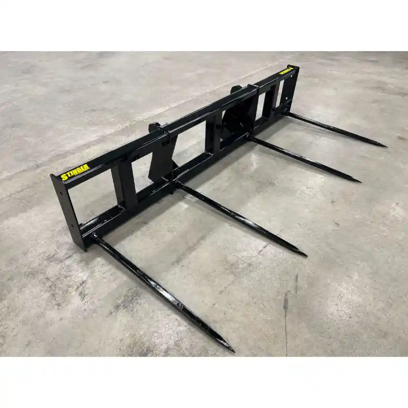 Black metal bale spear attachment with three long pointed spears resting on concrete floor