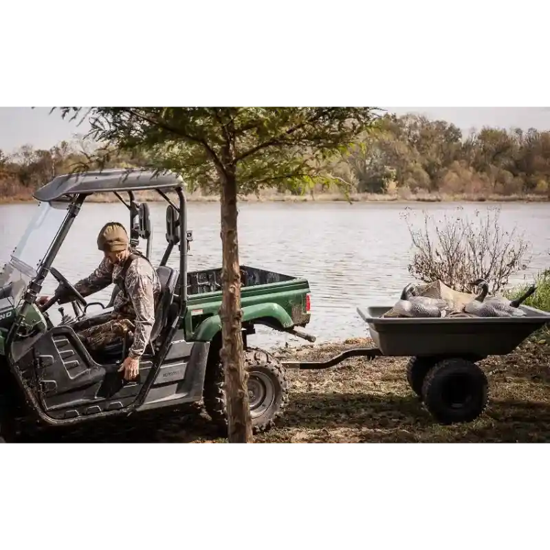 Utility vehicle pulling green Swisher 16 cu ft poly cart loaded with harvested fish, lakeside, gallery position 1
