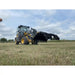 Yellow Deere loader with large black steel clam-style grapple attachment lowered over dry grass field under cloudy sky