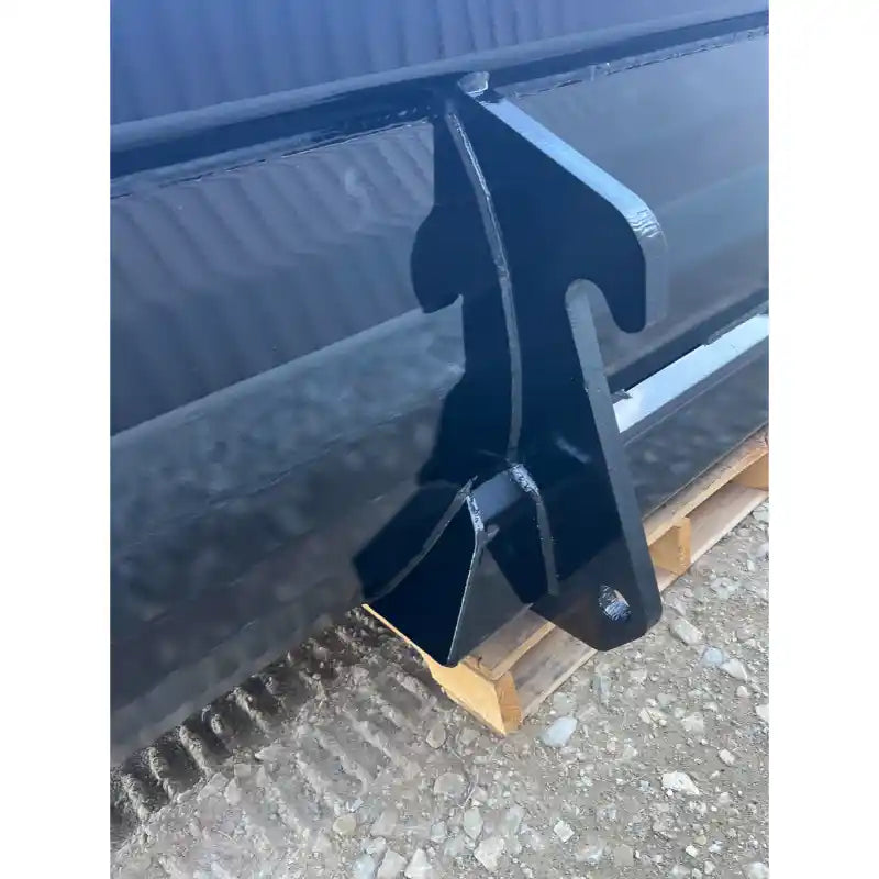 Close-up of black steel skid steer bucket attachment showing welds and reinforced mounting hook on gravel surface