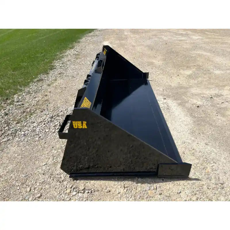 Black steel skid steer material bucket with smooth interior and visible "Made in USA" stencil on gravel surface outdoors