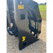 Close-up of black steel grapple attachment with hydraulic fittings and yellow "Made in USA" and logo markings on gravel outdoors