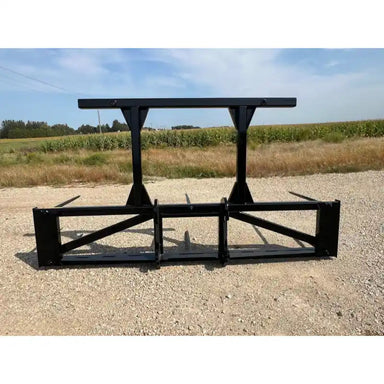 Black steel skid steer attachment with two vertical support arms and wide horizontal frame on gravel surface viewed from front angle