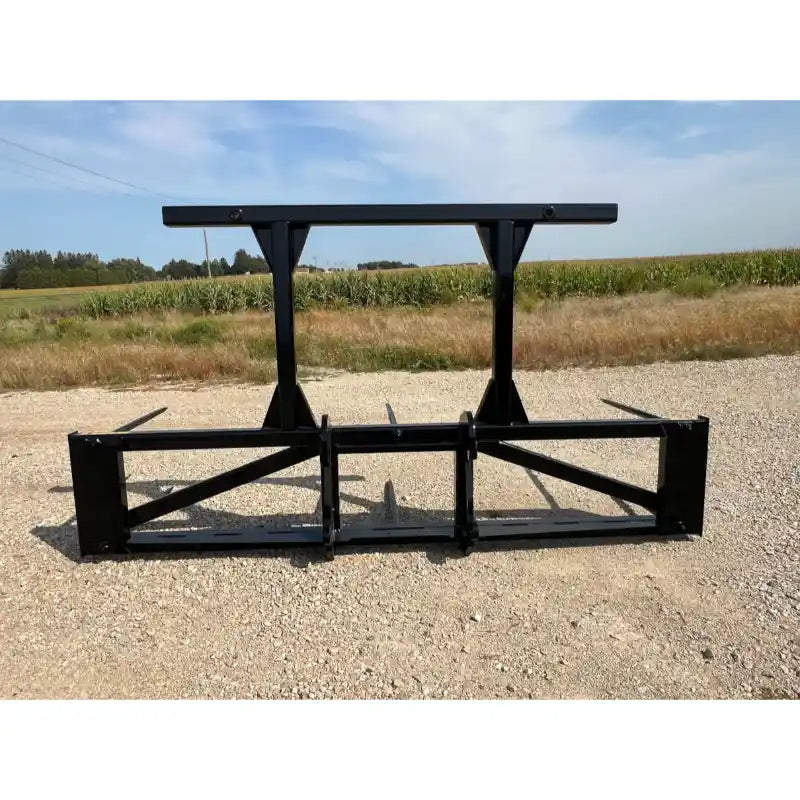 Black steel skid steer attachment with two vertical support arms and wide horizontal frame on gravel surface viewed from front angle