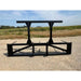 Black steel skid steer attachment with two vertical support arms and wide horizontal frame on gravel surface viewed from front angle