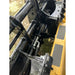 Close-up of black steel clam grapple attachment with hydraulic hoses connected to yellow skid steer loader outdoors