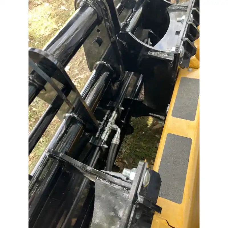 Close-up of black steel clam grapple attachment with hydraulic hoses connected to yellow skid steer loader outdoors