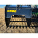 Black steel rock grapple with spaced flat tines and serrated upper jaw mounted on loader attachment over dry grass