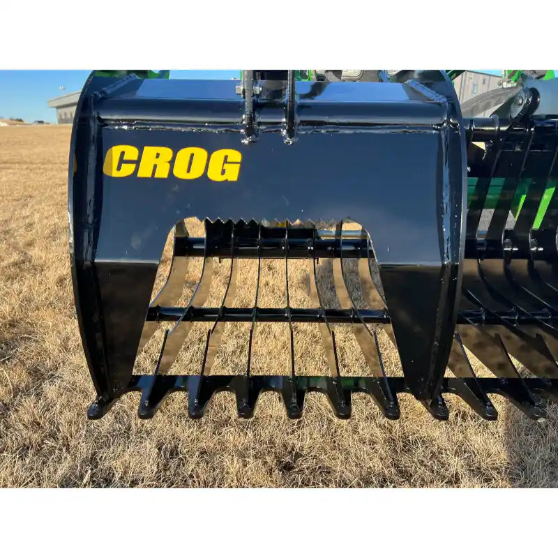 Black steel rock grapple with spaced flat tines and serrated upper jaw mounted on loader attachment over dry grass