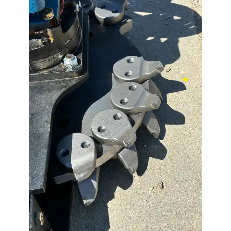Close-up of metal stump grinder teeth mounted on a black attachment frame on concrete surface