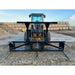 Black steel bale spear skid steer attachment with five pointed tines mounted on yellow loader outdoors on dirt surface