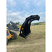 Yellow loader with black multi-tine clam-style grapple attachment raised over grassy field under partly cloudy sky