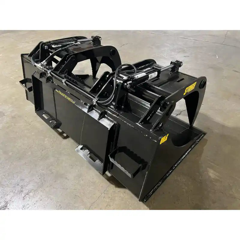 Black steel demolition grapple attachment with dual hydraulic cylinders and clamp arms on indoor concrete surface