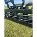 Close-up of black hydraulic skid steer attachment with metal bars and bolts resting on grass outdoors
