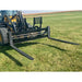 Black steel pallet fork attachment with adjustable tines mounted on a yellow skid steer on grassy field