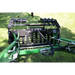 Close-up of black steel grapple attachment with hydraulic hoses mounted on green compact tractor on grass outdoors